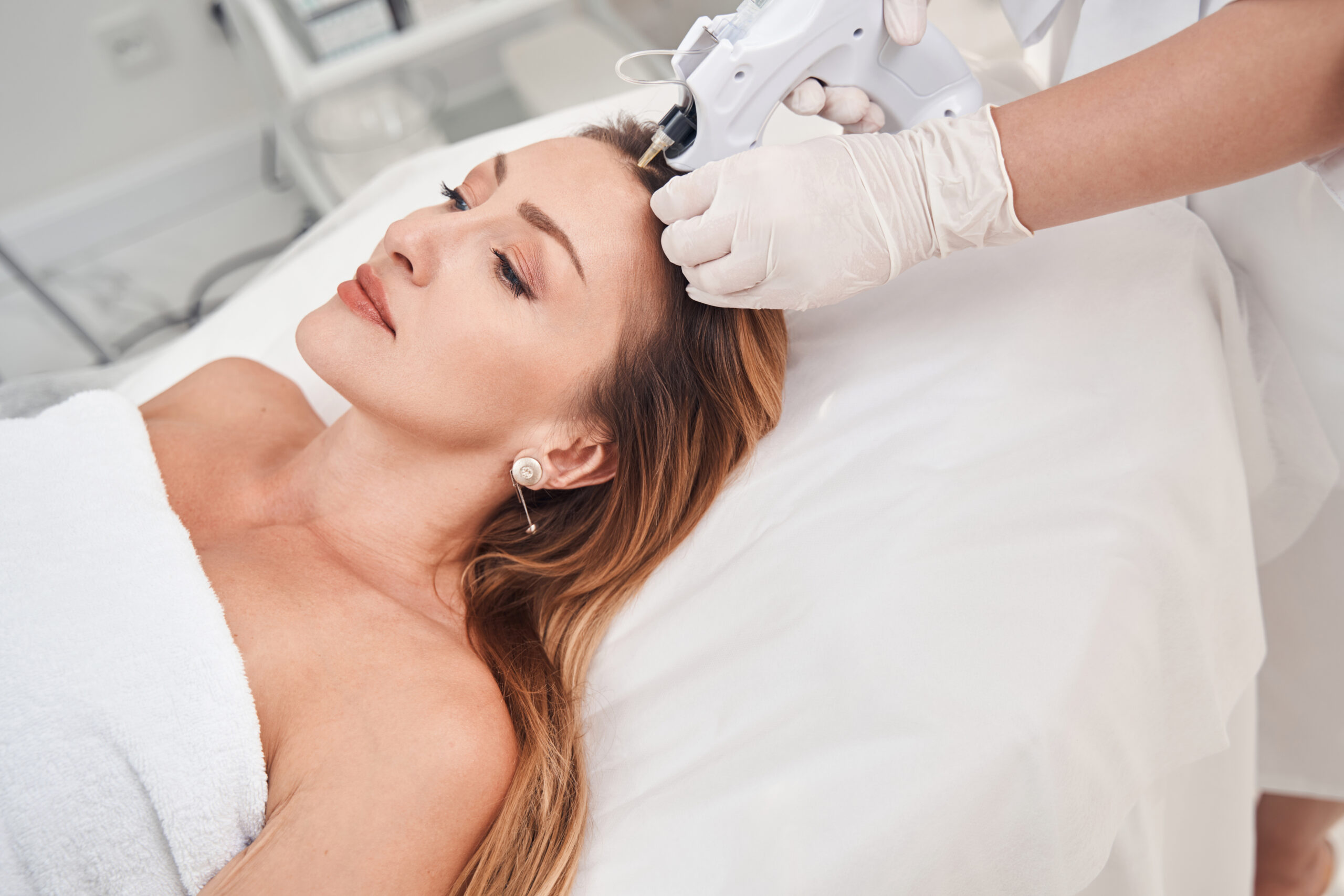 Top view of pretty female lying on couch while cosmetologist is doing injections in her head